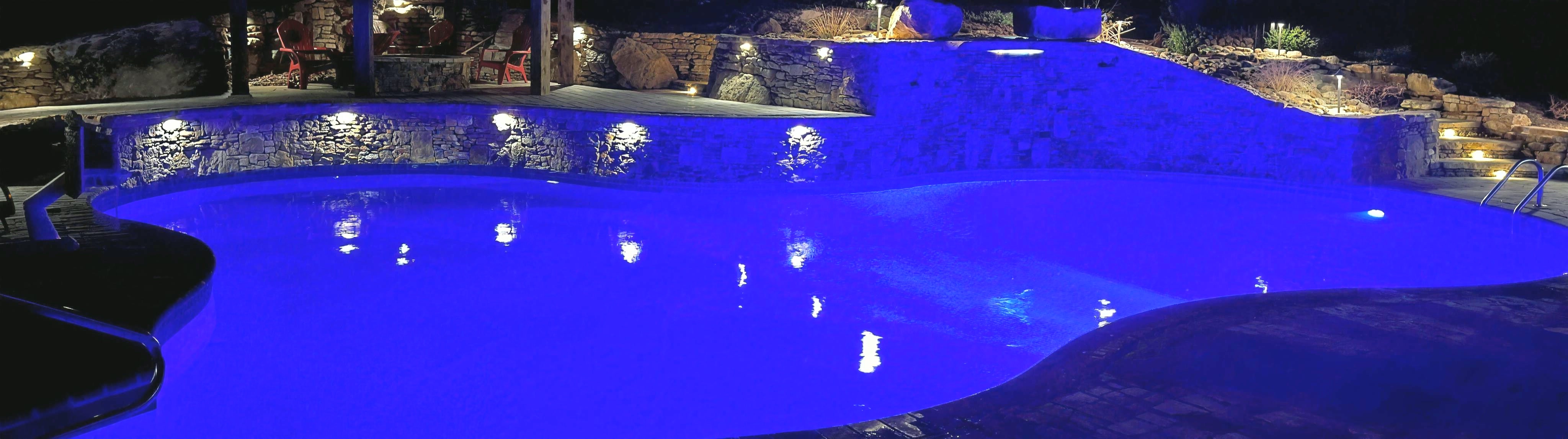 Gunite pool with stacked-stone wall, lit at night